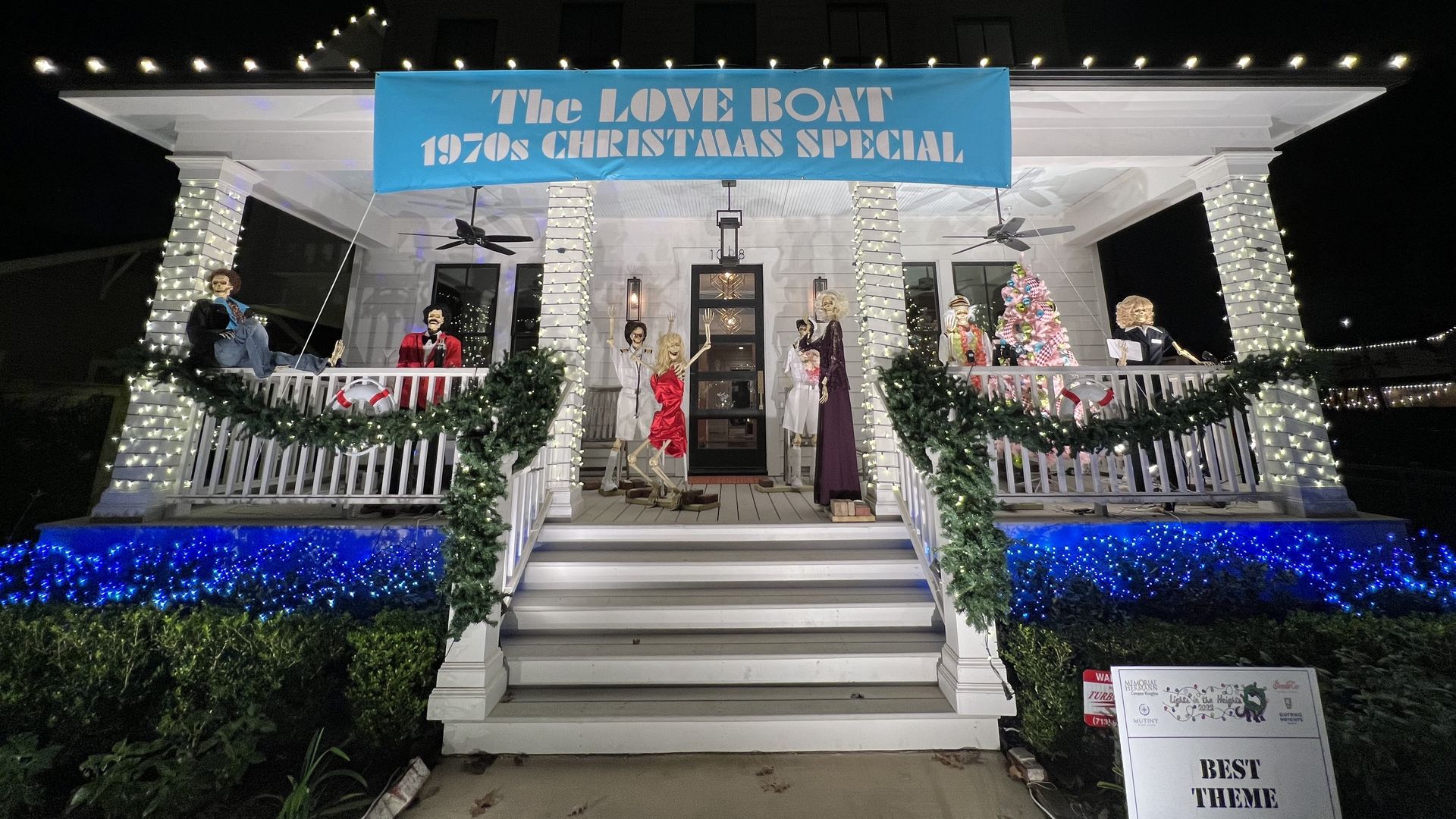 A white house is decorated with holiday lights and skeletons