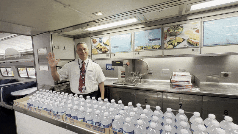 Image shows a man waving in the cafe of a train.
