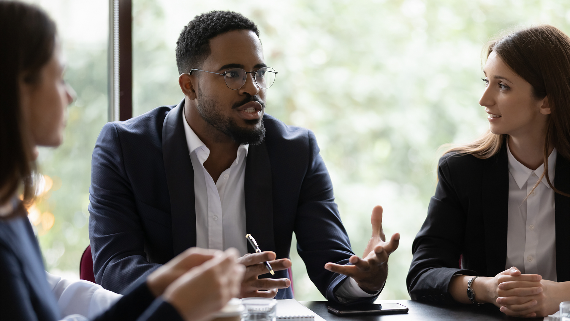 Two women and one man speak in a conference room.