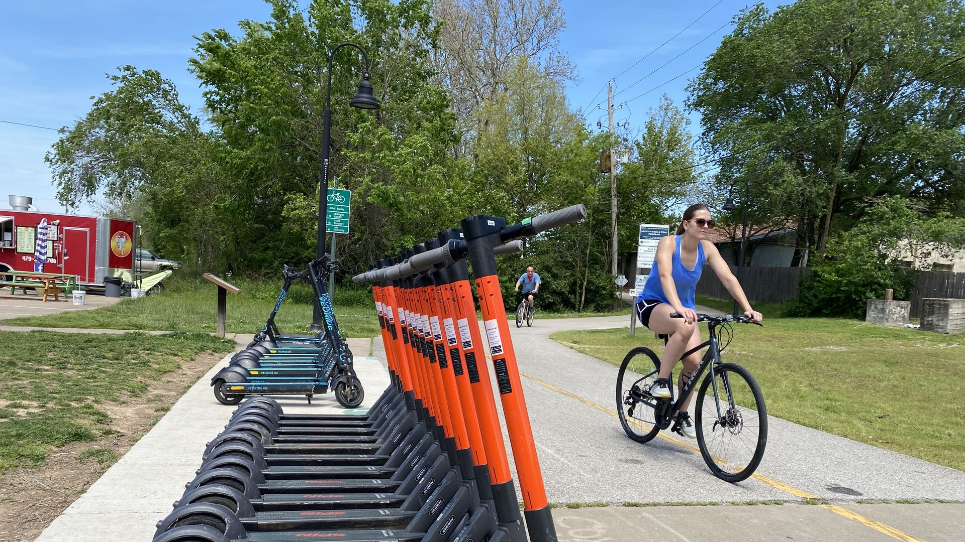 Photo of a woman riding a bike by a row of electric scooters. 