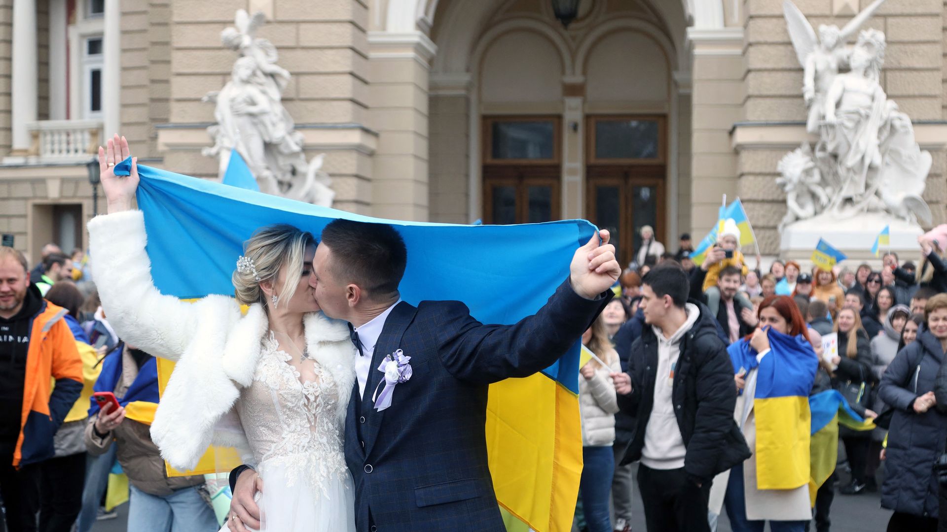 Newlyweds, holding Ukrainian flag, kiss as they celebrate the liberation of their native town.