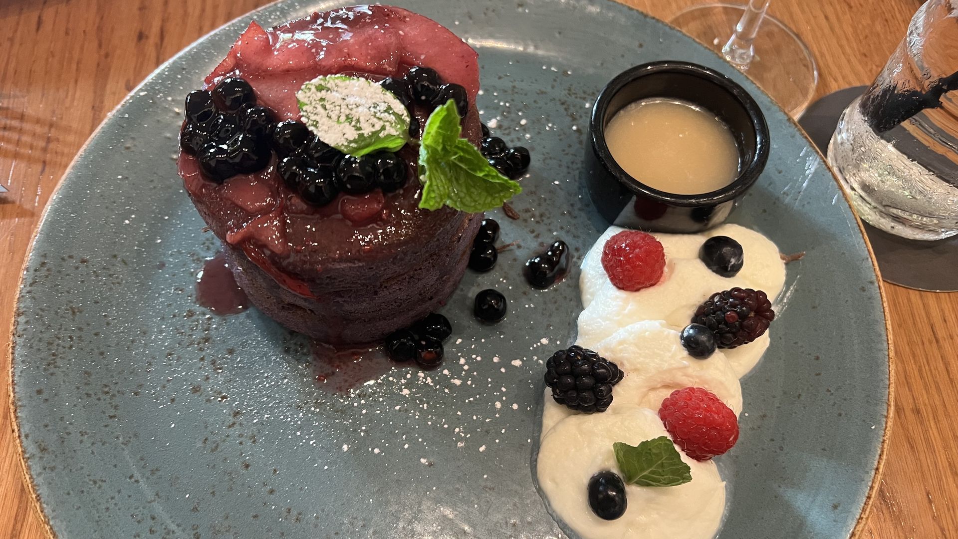 Ube pancake topped with black tapioca pearls, fruit compote, and mint leaves on a blue plate, served with whipped cream garnished with berries. 