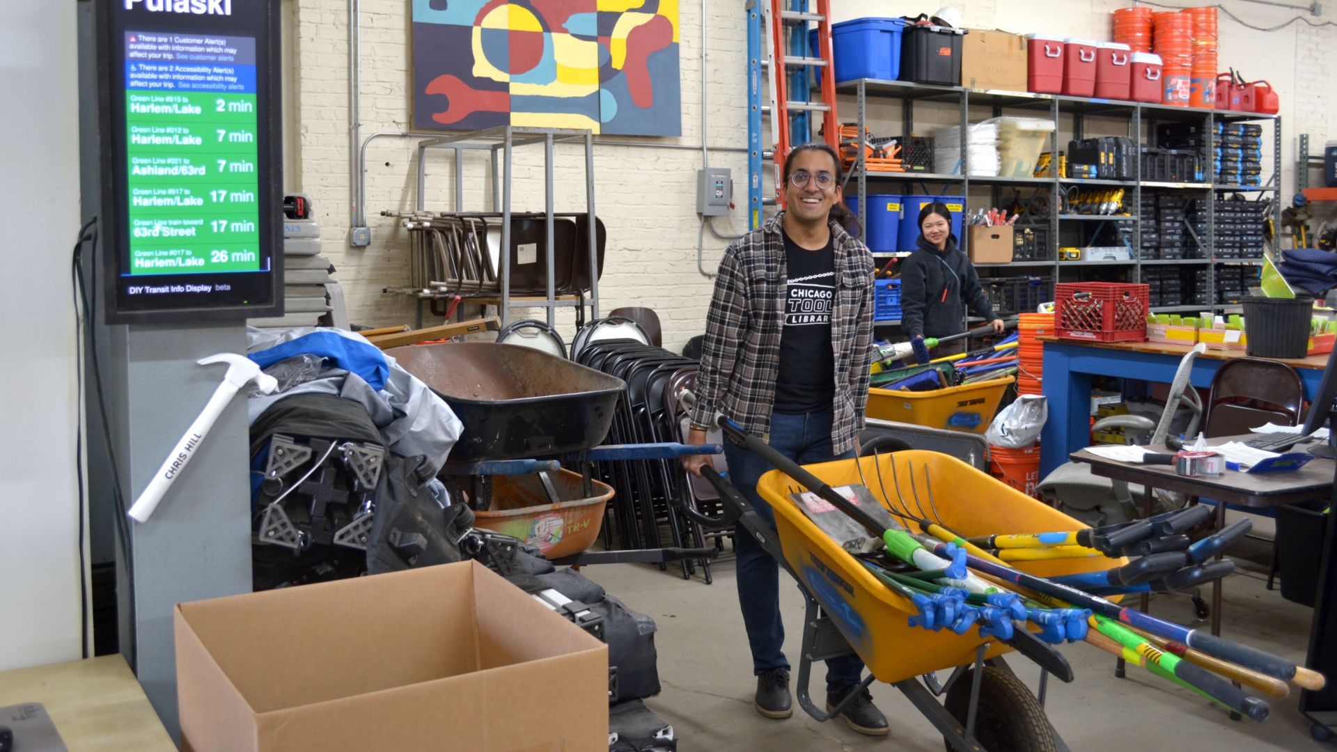 Two people with a wheelbarrow full of tools.