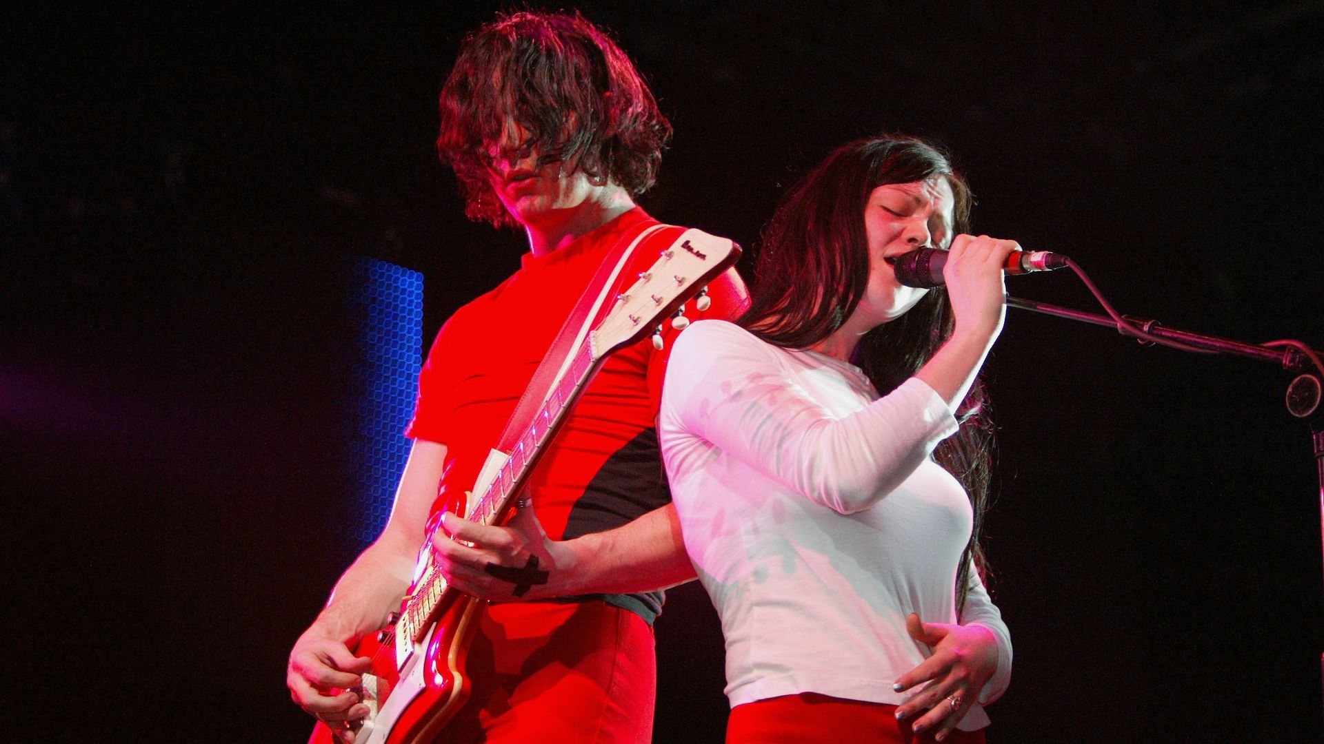 Jack and Meg White of The White Stripes perform on stage in orange and white attire.