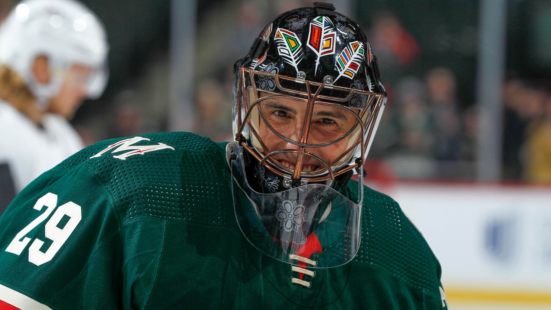 A hockey goaltender pictured from the chest up in a forest green jersey with the number 29 stiched onto the arm and a black helmet on his head