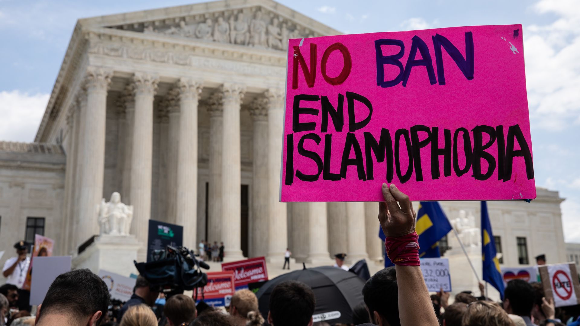 Photo of an arm raising a pink sign that says "No ban end Islamophobia" at a protest outside the Supreme Court