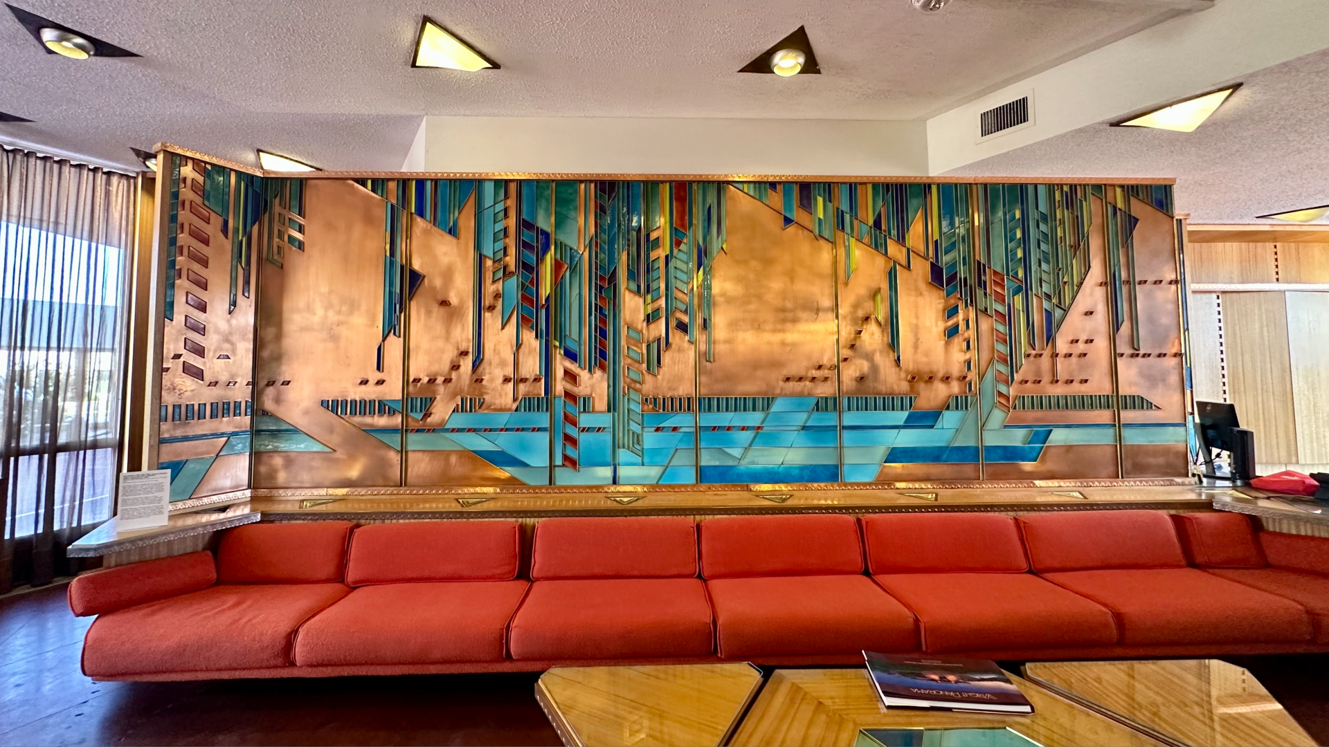 A photo of a long couch and copper wall hanging inside Price Tower