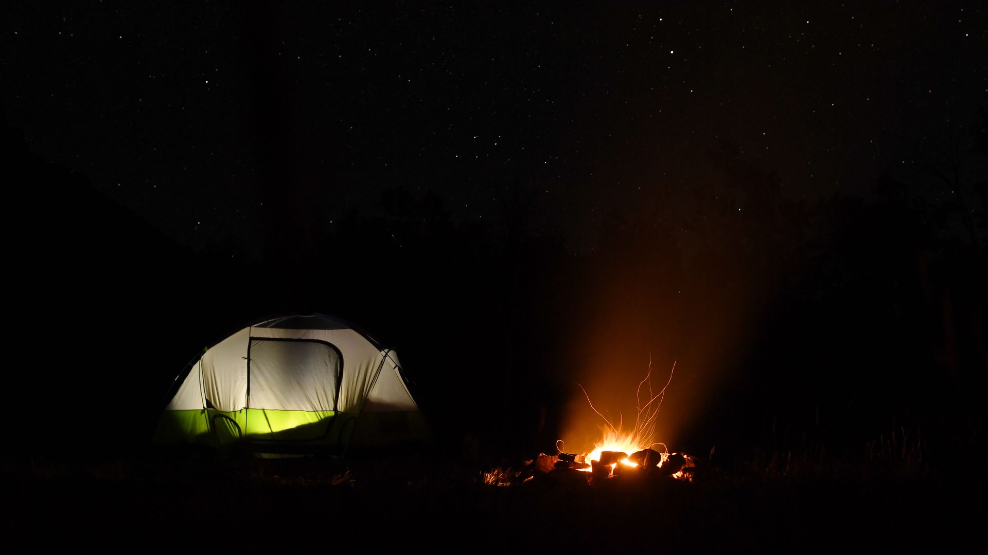 A campfire glows in a fire ring with campers in a tent nearby on Kebler Pass outside of Crested Butte. 