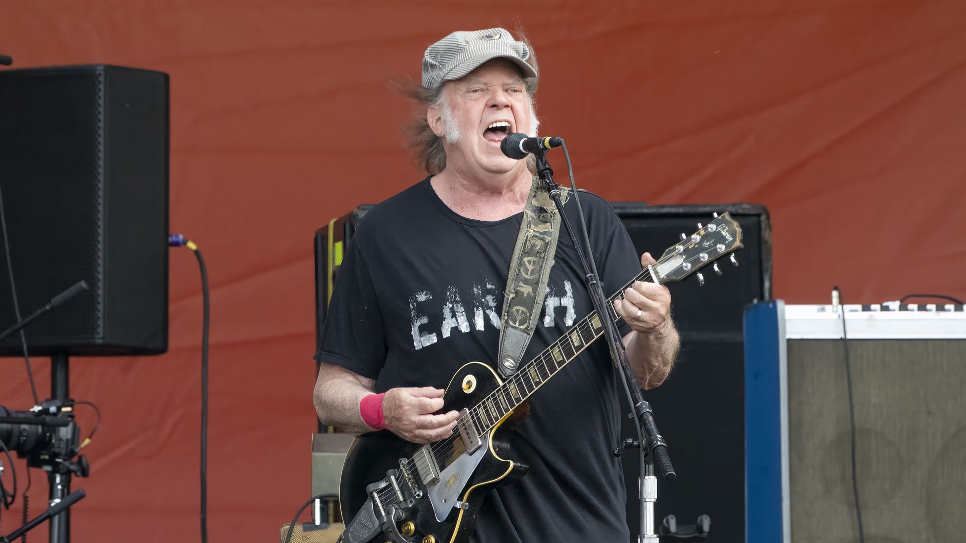 Neil Young performs on stage with an electric guitar while singing into a microphone. 