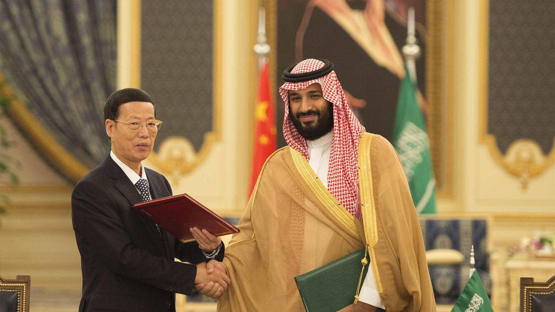 In this image, Saudi Crown Prince Mohammed bin Salman shakes hands with a Chinese diplomat in front of the Chinese and Saudi Arabian flags.