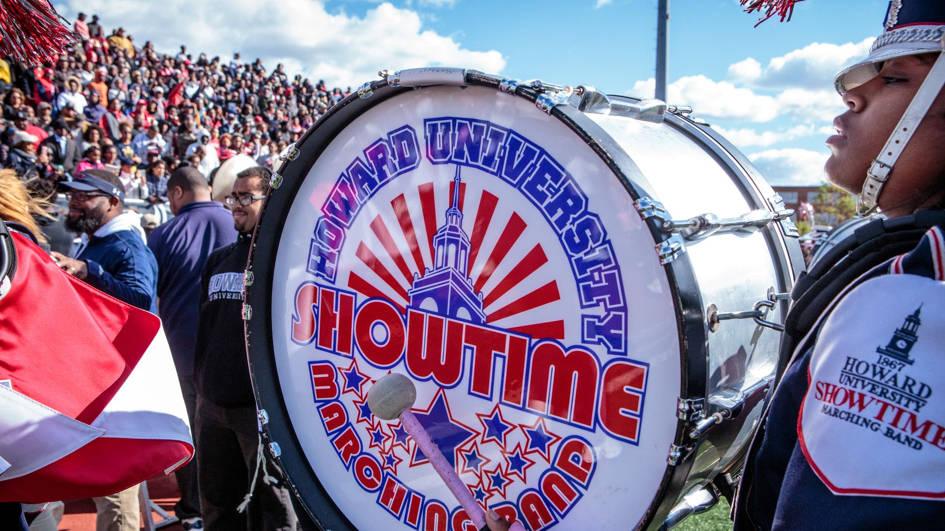 A closeup of a member of Howard University's marching band who's holding a drum that says "showtime" in red and blue letters.