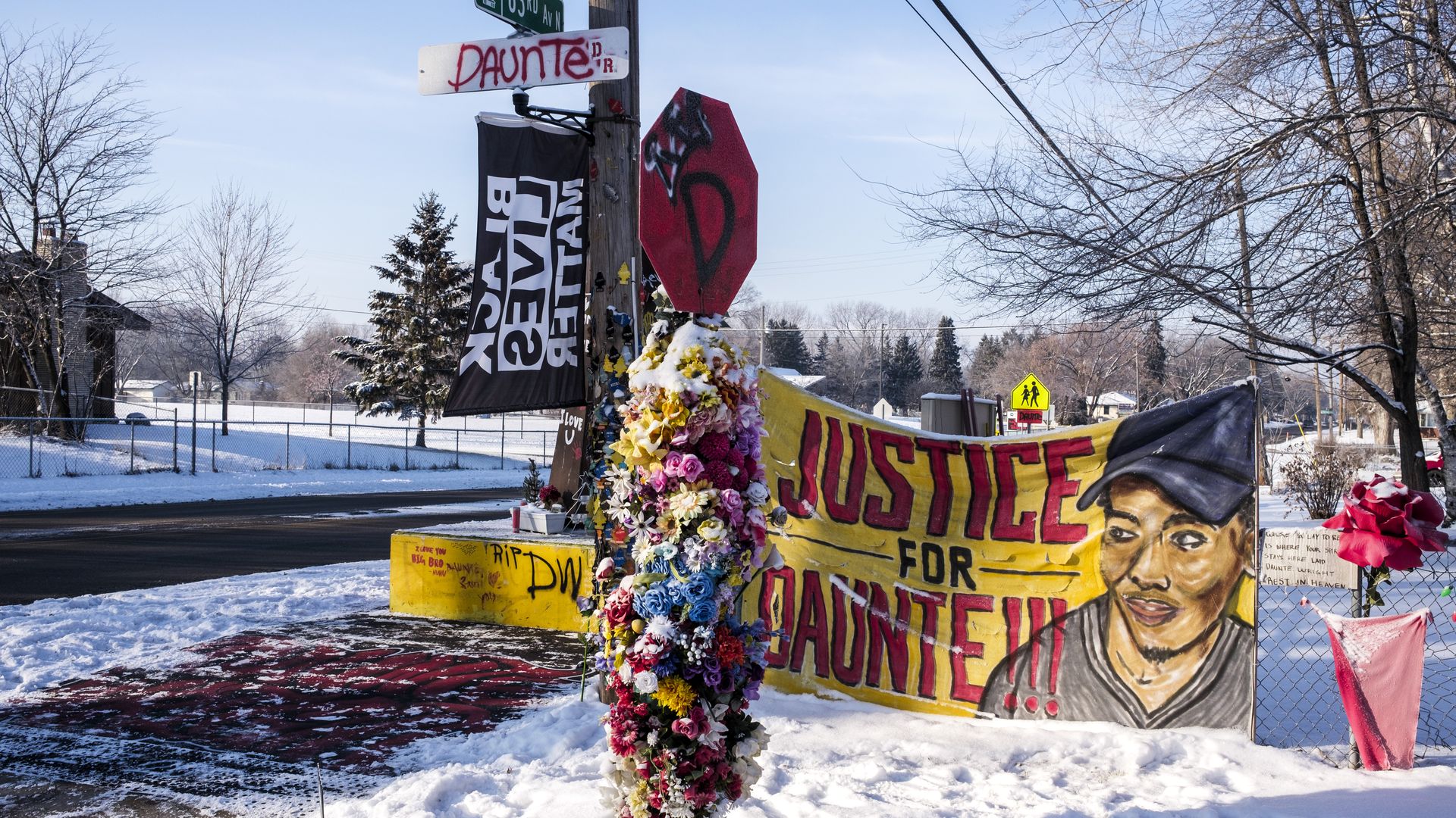 Picture of a yellow sign that says "justice for daunte" along with a BLM flag and flowers