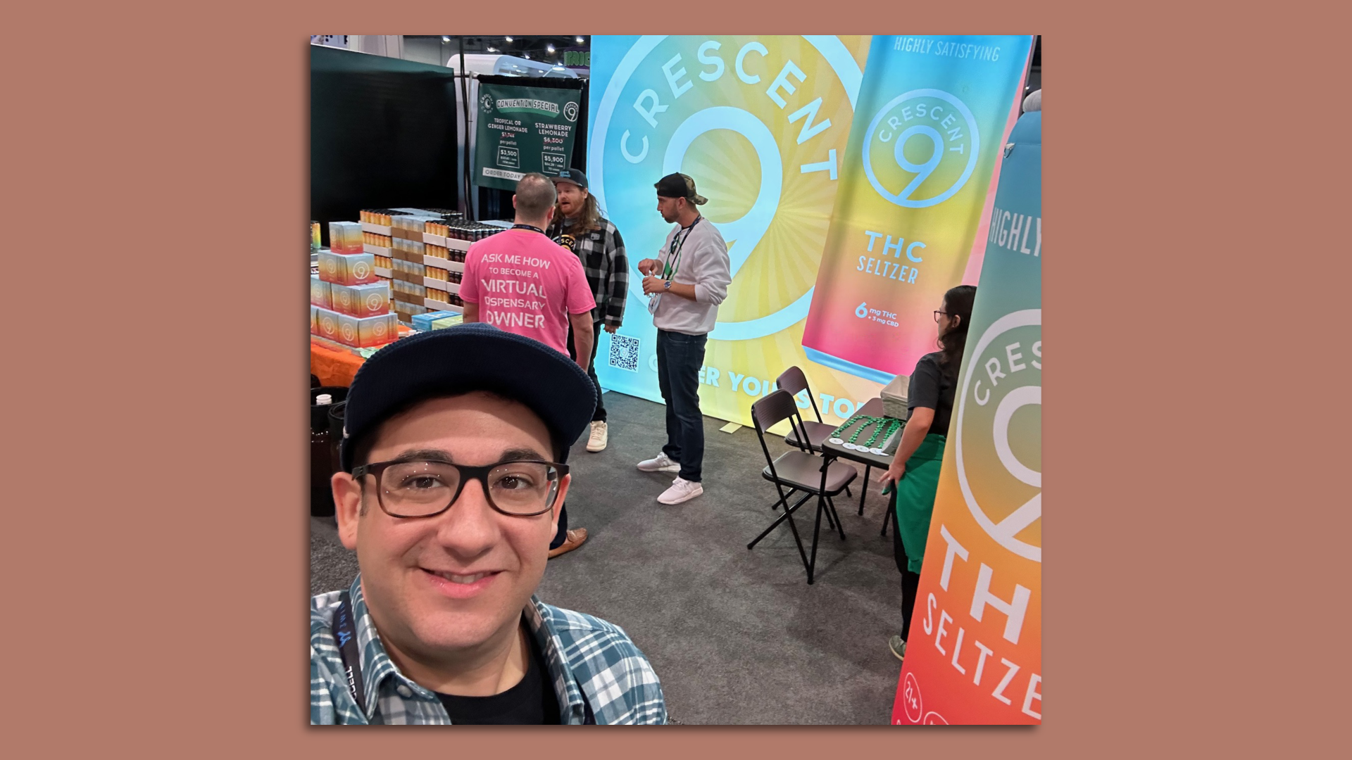 David Reich is seen in a selfie. He smiles while a conference booth for Crescent 9 is seen behind him. The booth has cans of the beverage and large colorful logos.