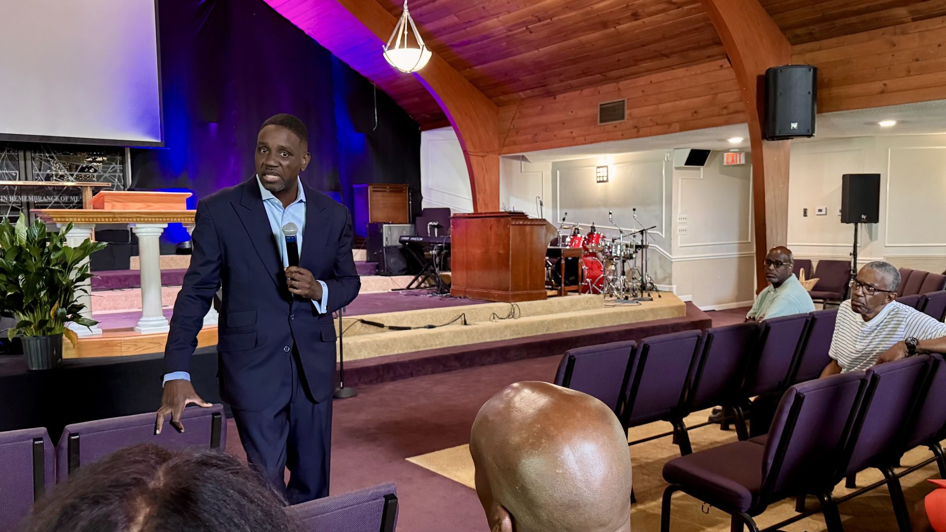 Kinloch holding a microphone speaks to seated attendees in a church. 