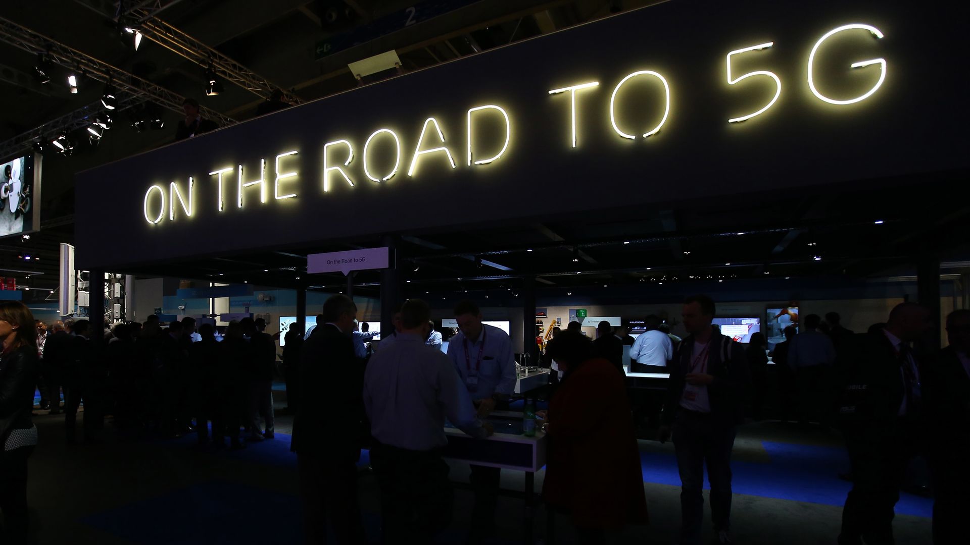 A neon sign at a conference reads "On The Road To 5G"