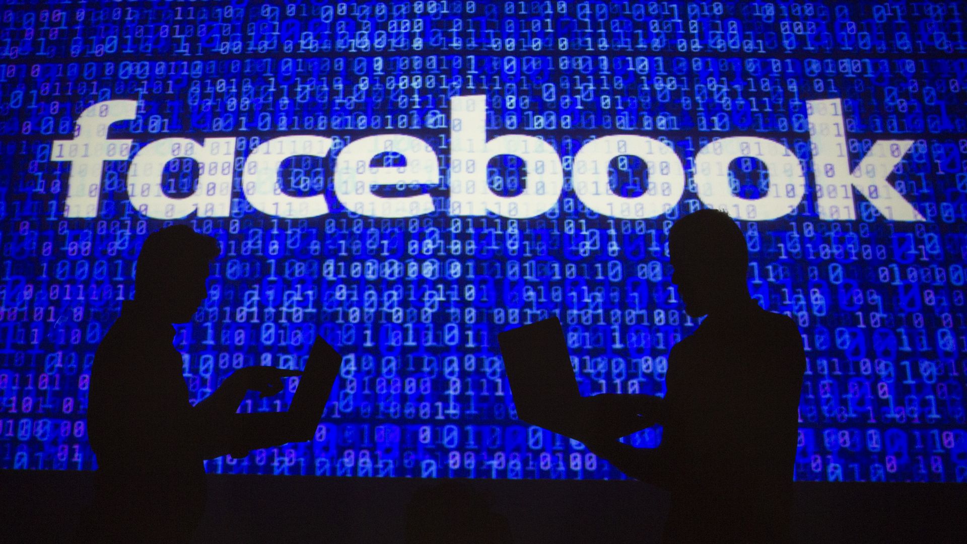 Two people silhouetted in front of Facebook logo