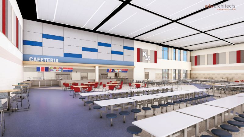 Spacious cafeteria with white and blue ceiling panels, a serving counter labeled CAFETERIA, red and gray chairs, and tables with attached blue stools, featuring NM initials on a wall.