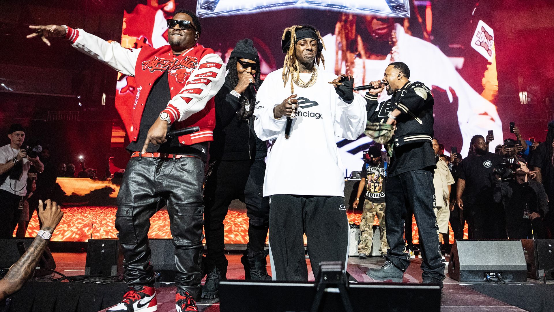 Four people perform onstage with microphones. Lil Wayne is at the center smoking a blunt.