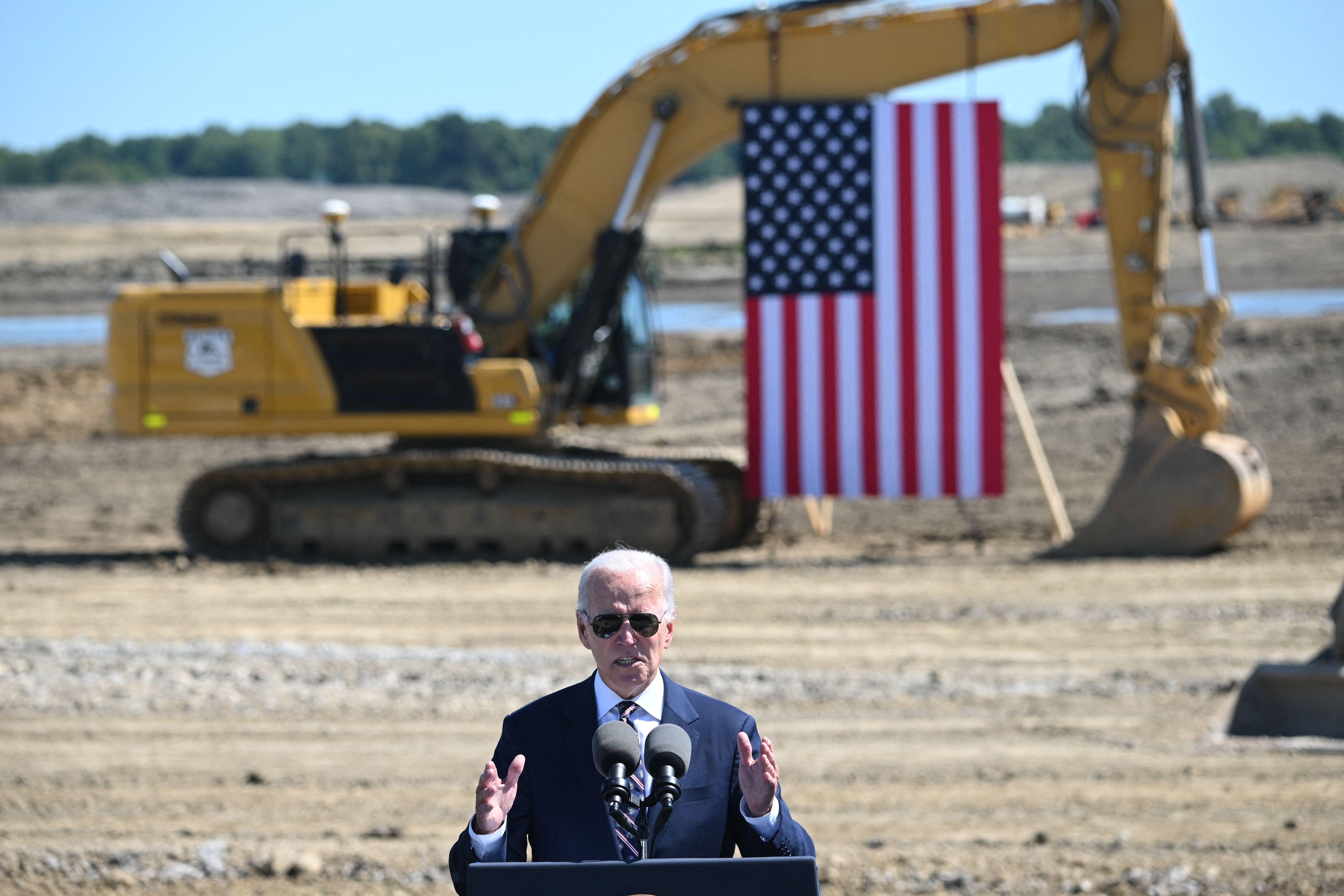 President Biden speaking in front of a tractor that holds an American flag.