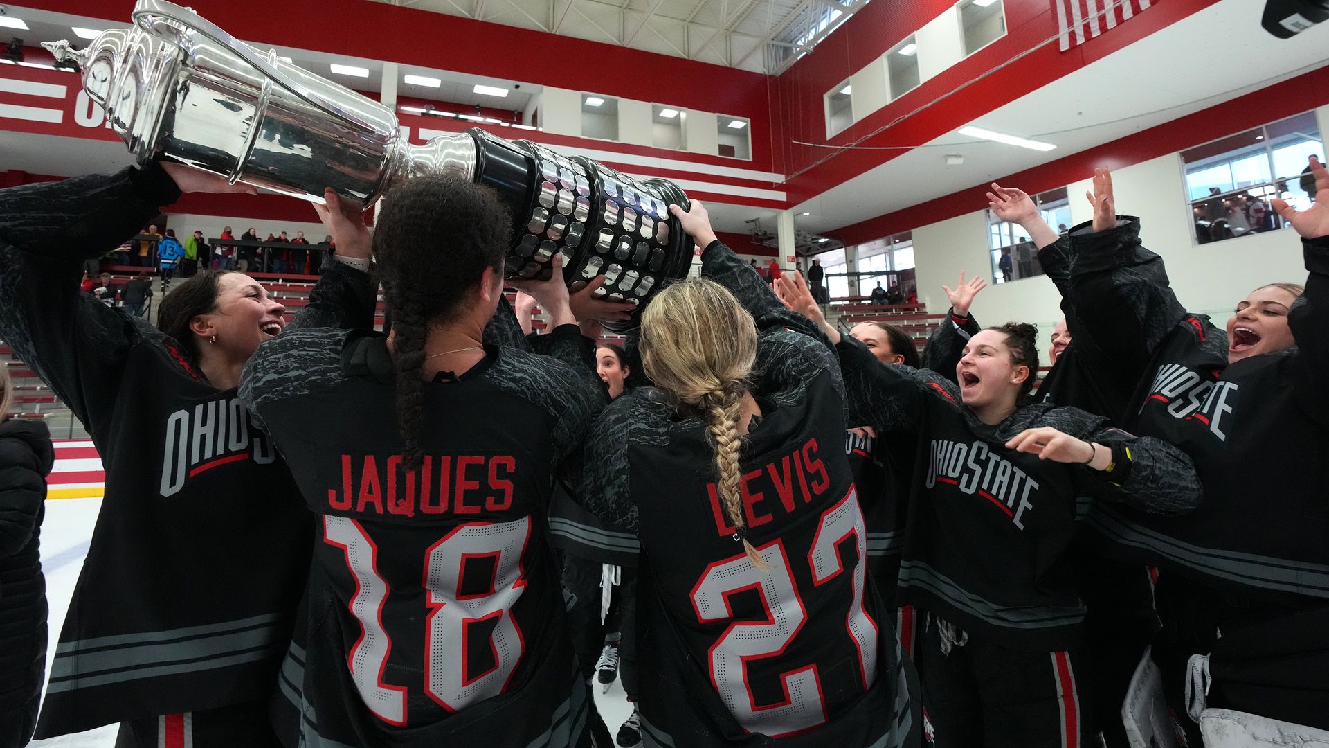 Ohio State women's hockey players hoist a trophy after winning the conference title.