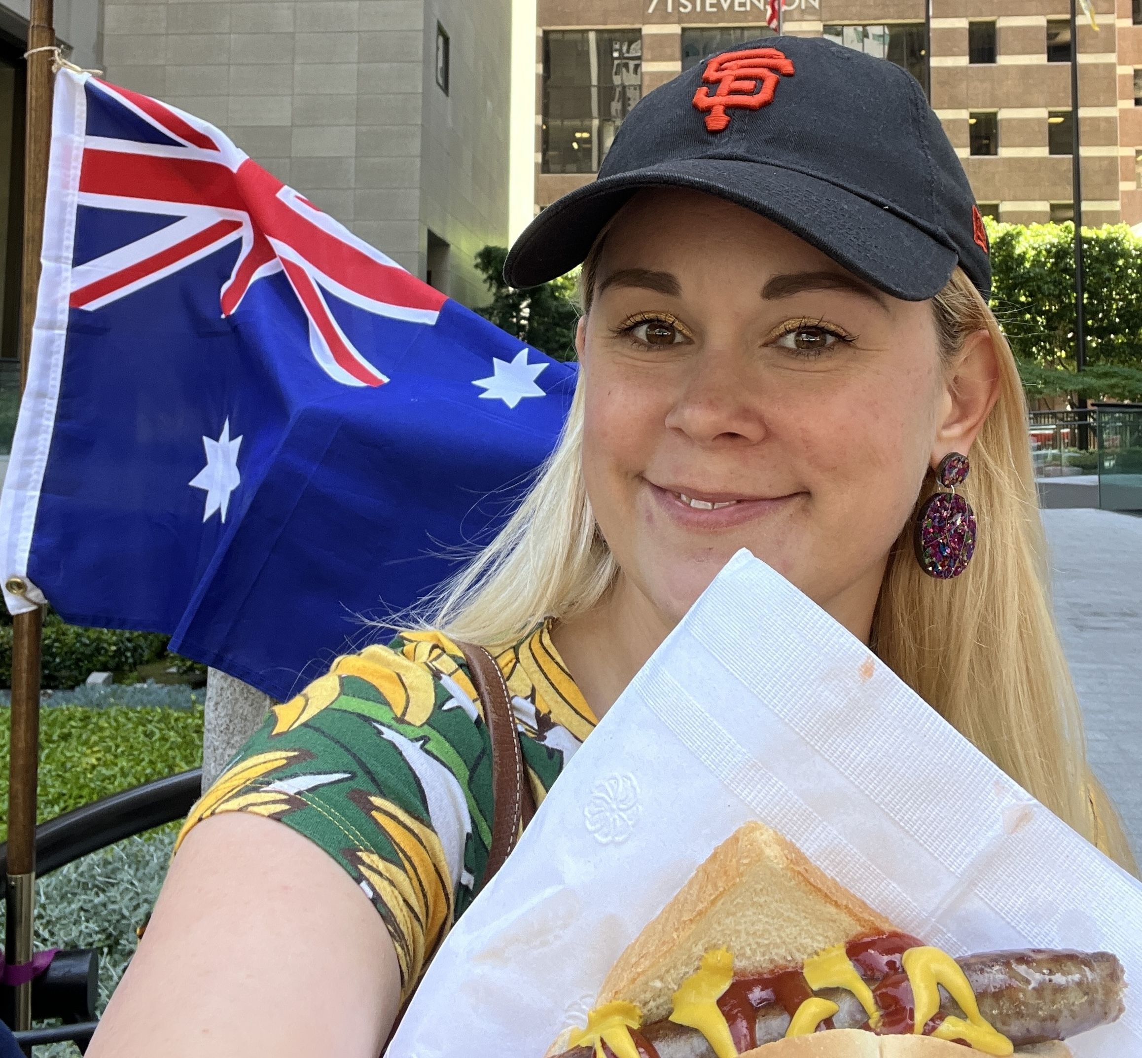 Photo of a blonde woman holding a sausage while an Australian flag flies behind her