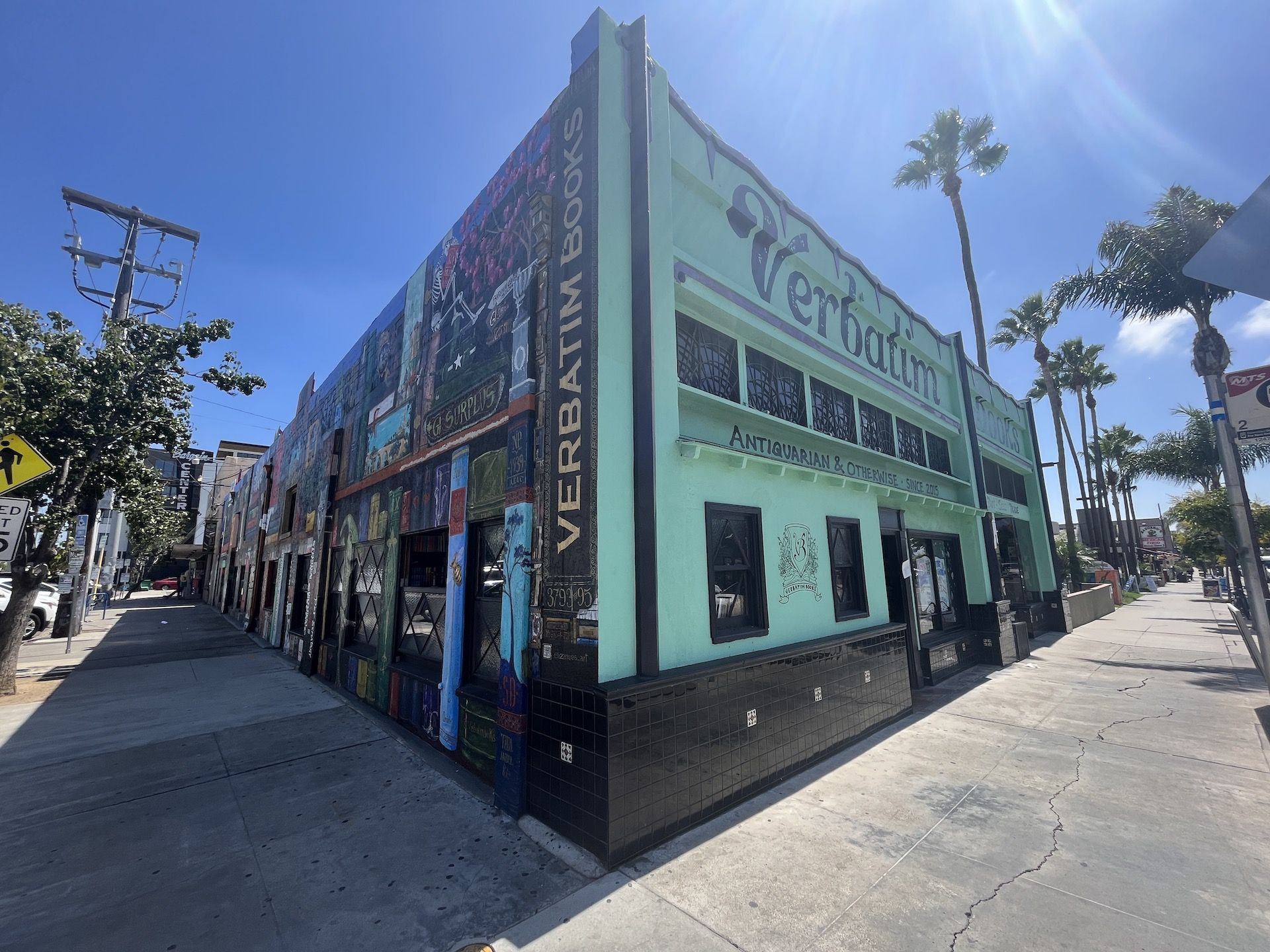 Streetview of a bookstore painted with a giant bookshelf mural on one side and bright teal on the other. 