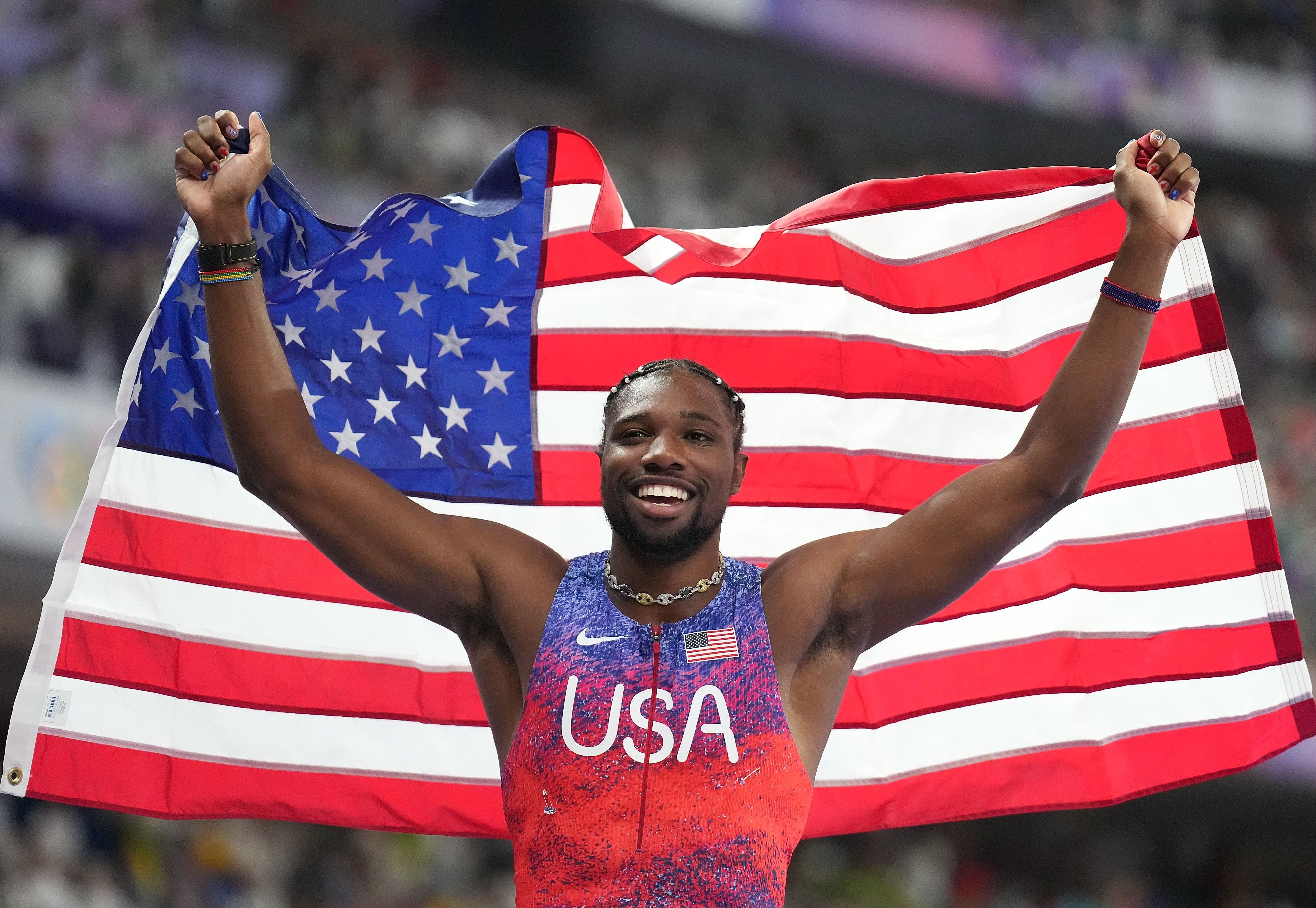 Olympian Noah Lyles holds an American flag over his head.