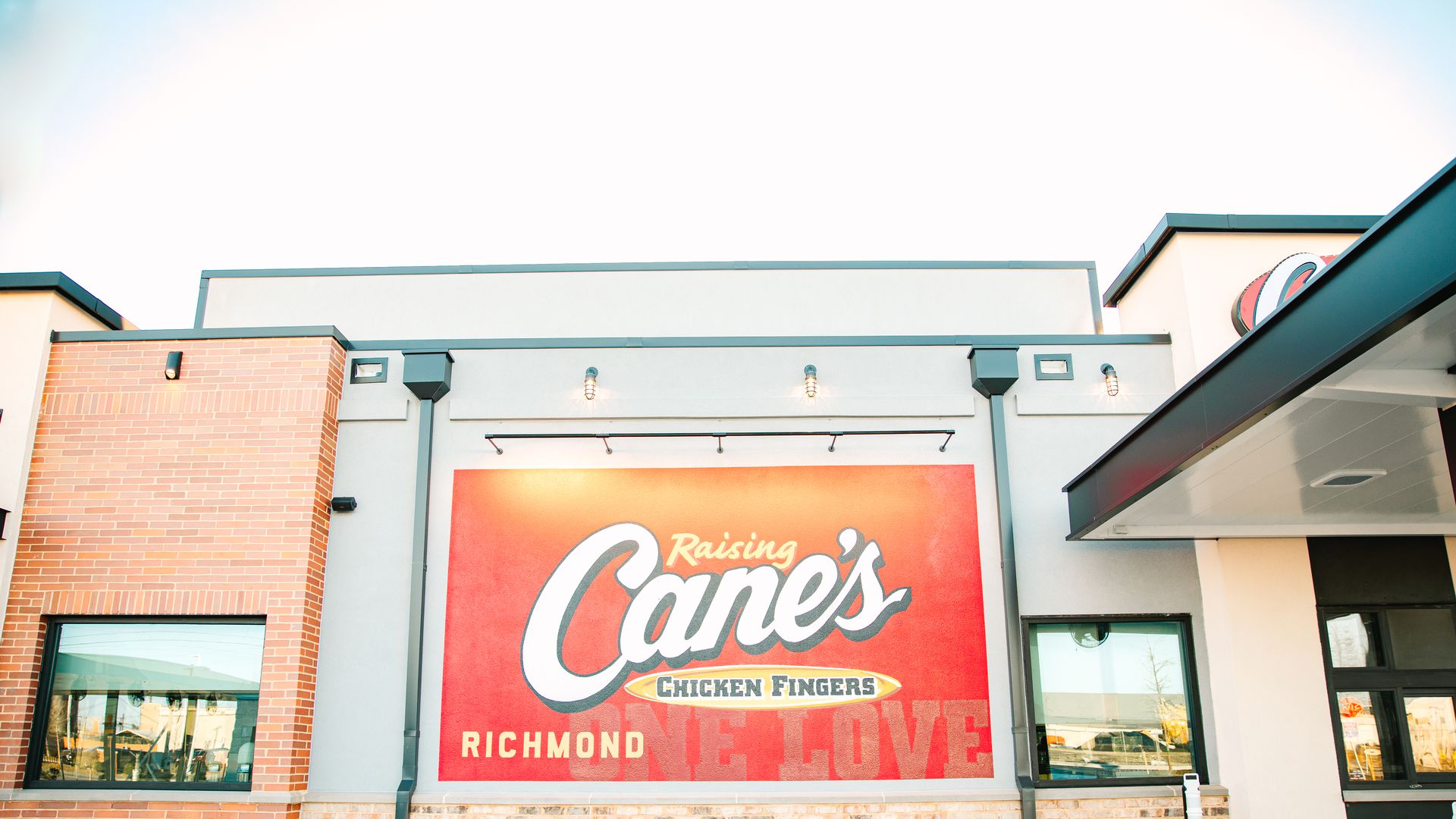 A pic of Raising Cane's Richmond with a red sign that says "Raising Cane's Chicken Fingers" and Richmond in the left corner.
