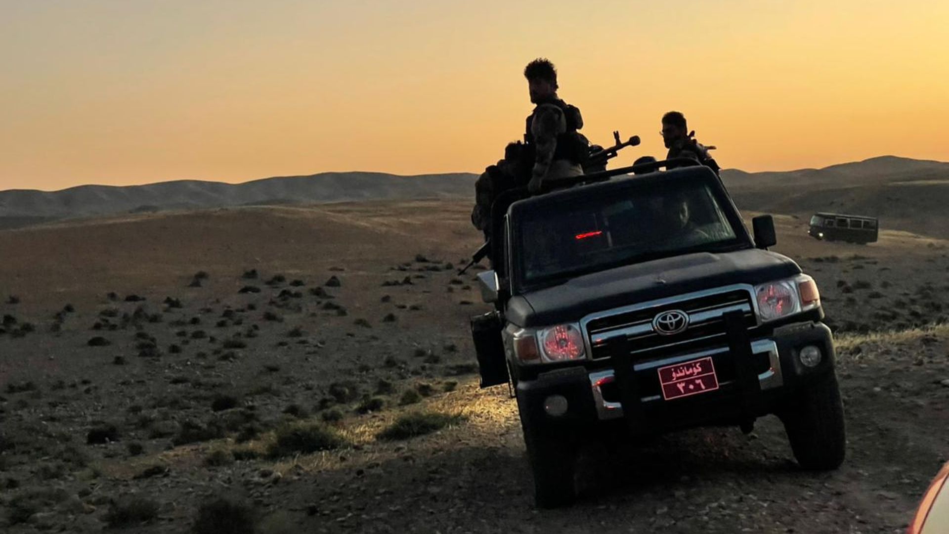 Photo of a military vehicle with soldiers sitting in it as it drives in a desert area