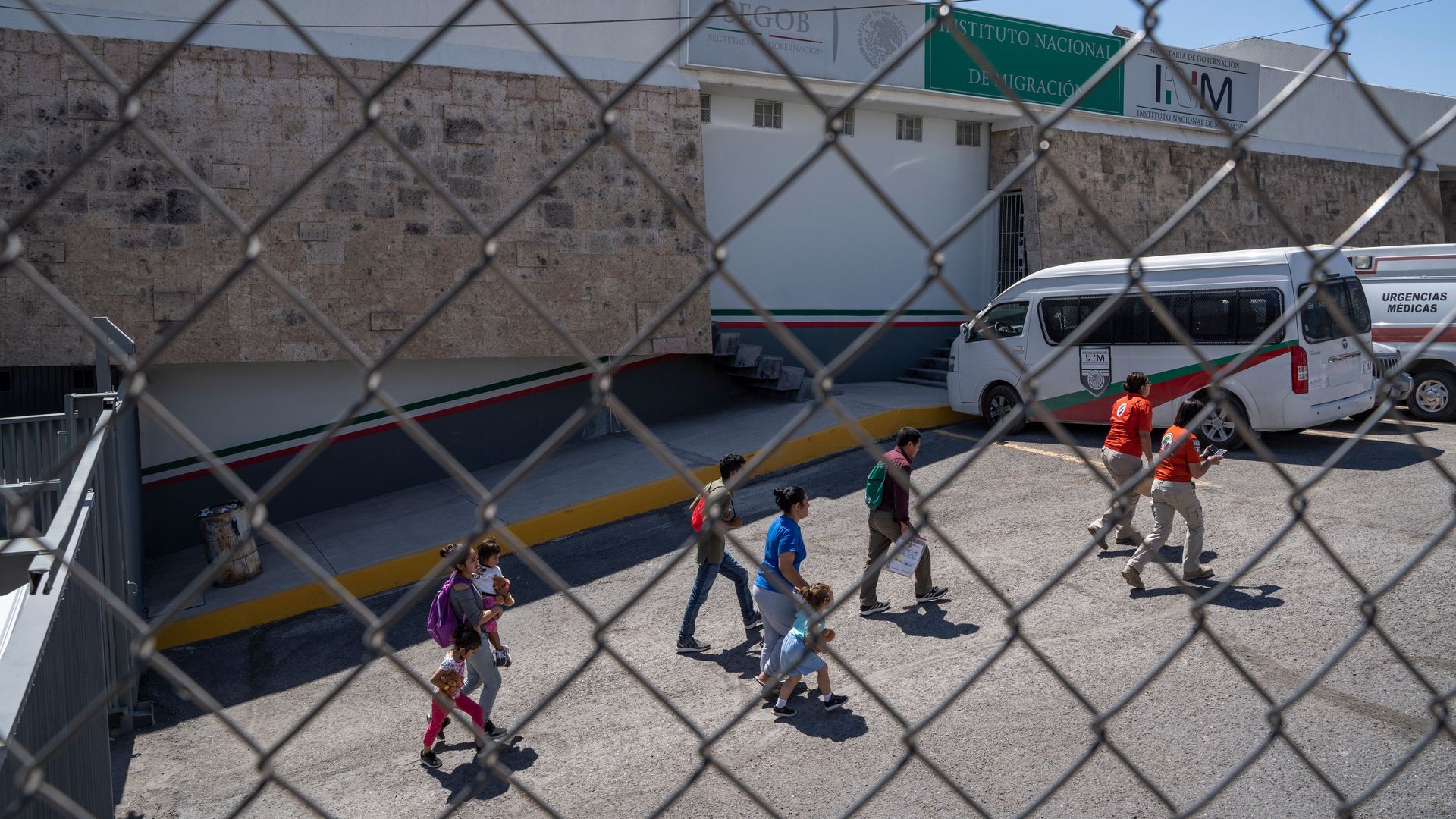 Migrants are led out of the National Institue of Migration in downtown Ciudad Juarez, Mexico. Seen through a chain link fence.