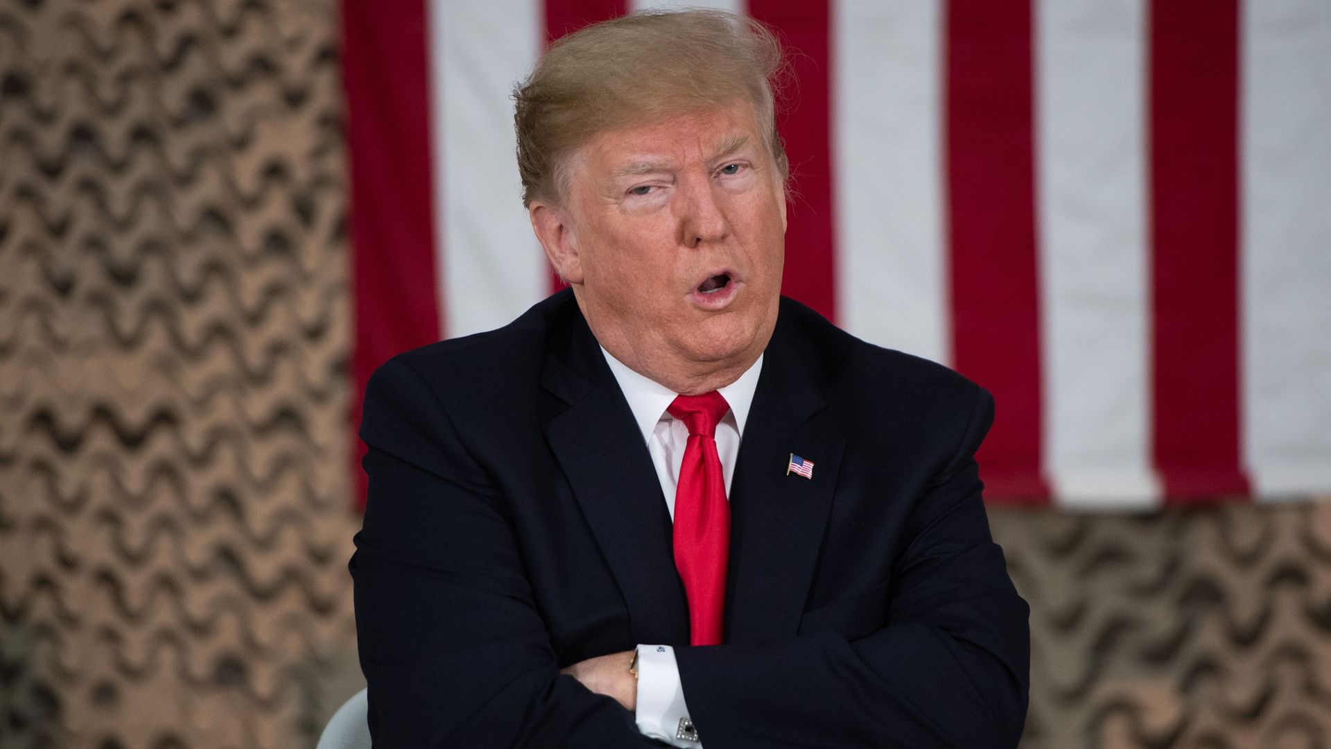 Donald Trump with his arms crossed and talking but looking unhappy