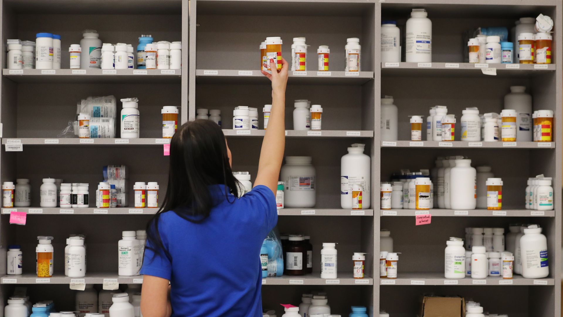A pharmacist reaches for a prescription drug bottle in a pharmacy.