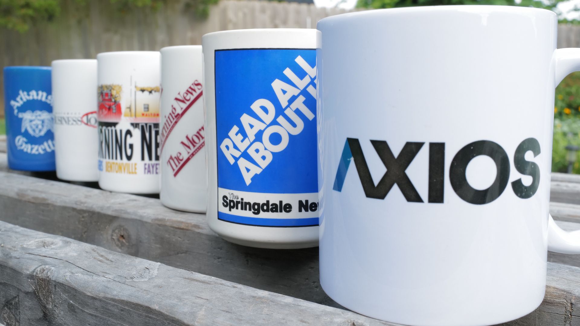 A photo of several coffee mugs advertising various news papers and news outlets.