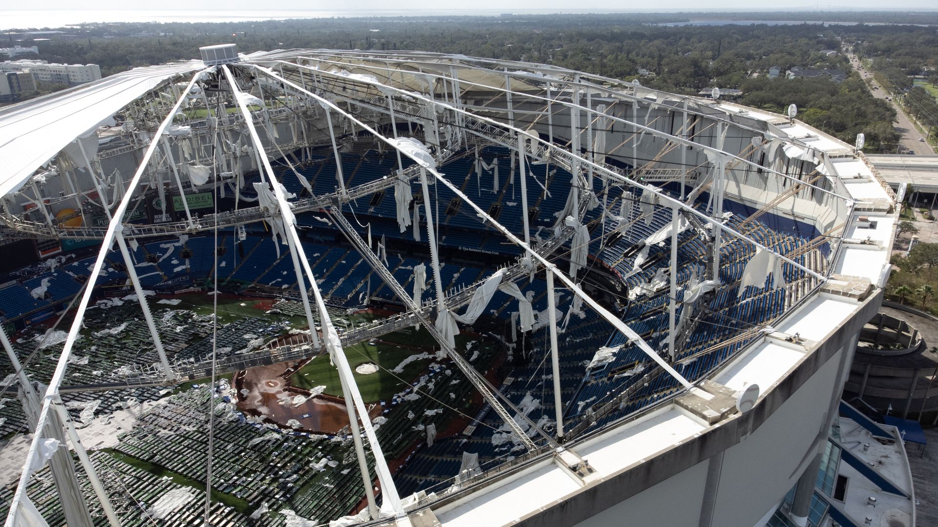 An image looking into a baseball stadium through the tatters and skeleton of what used to be a dome-shaped roof.