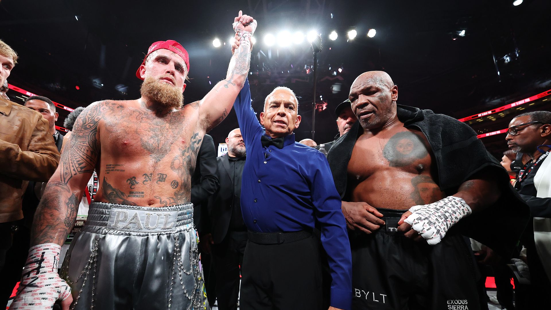 A referee lifts the hands of a boxer in gray trunks next to a boxer in black trunks