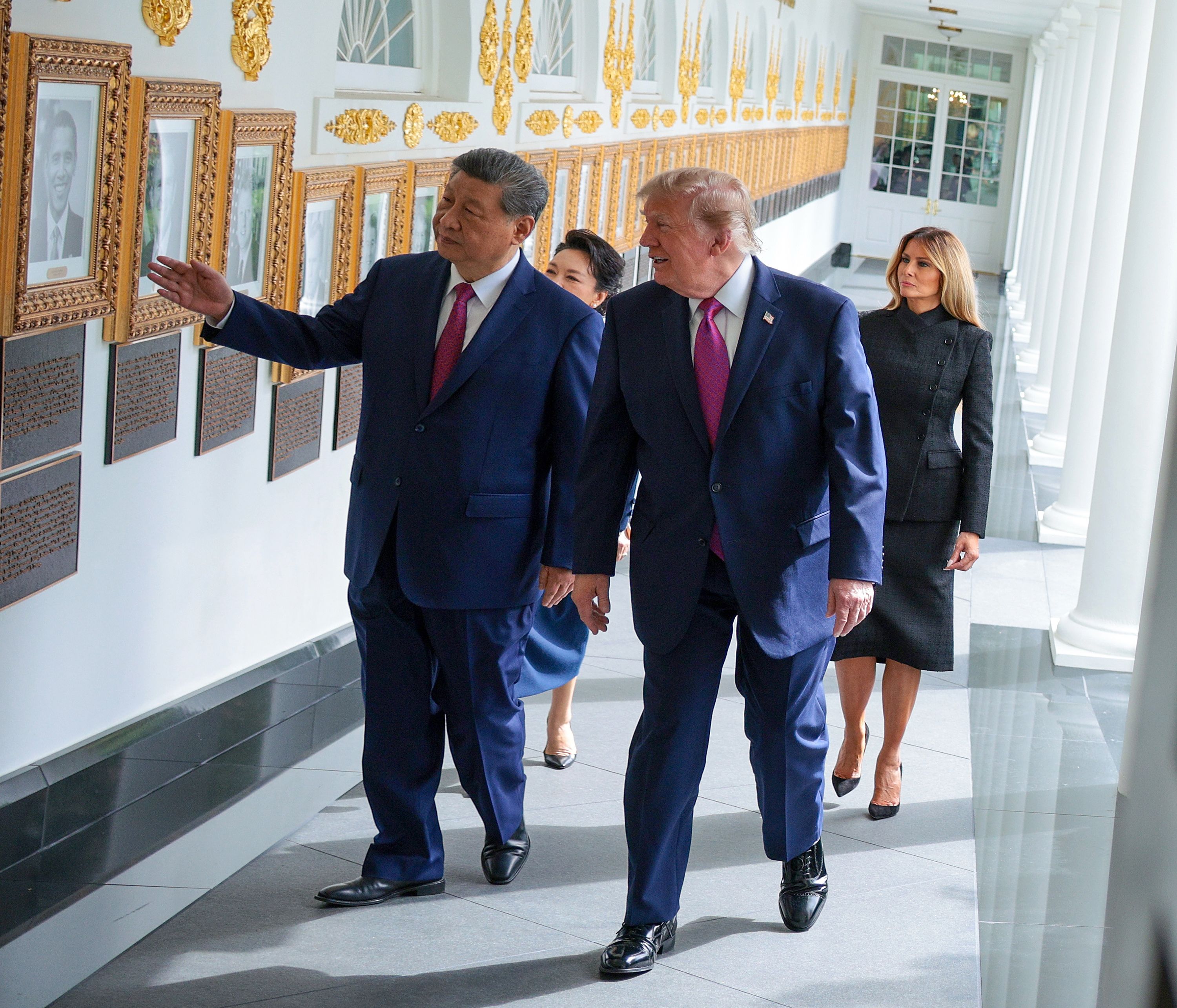 Chinese President Xi Jinping — wearing a dark blue suit, a white collared shirt and a red tie — gestures to a gold-framed photo of former President Barack Obama while walking outside the White House with President Trump, who is wearing a dark blue suit, a white collared shirt and a pink tie.