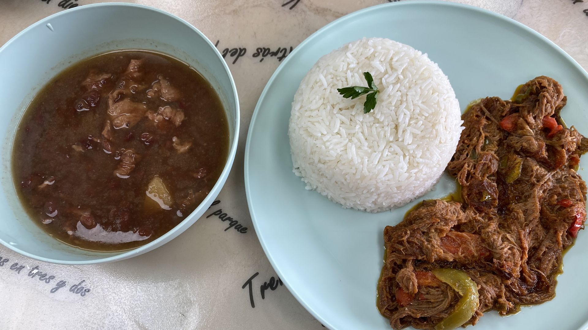 A bowl of stew next to a plate of white rice and shredded beef. 