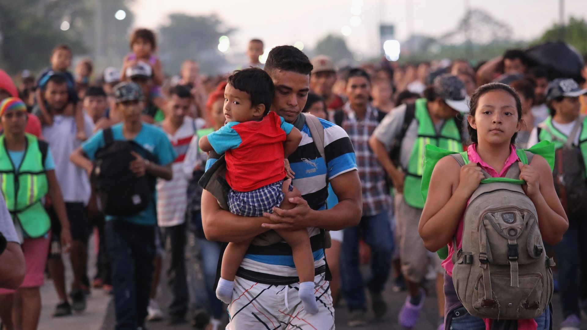 Man carrying young boy walks ahead of a caravan of people.