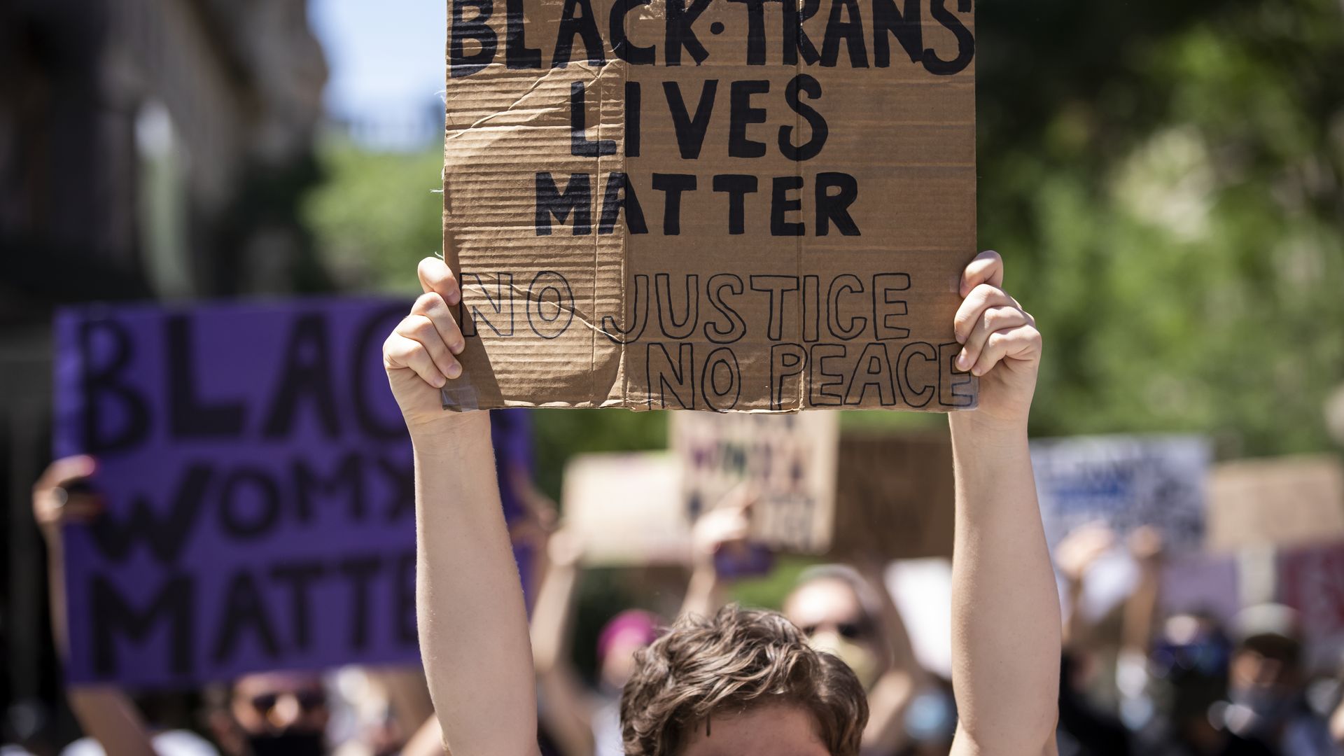 A Caucasian protester holds a homemade sign made from a box that says, "Black Trans Lives Matter No Justice No Peace" during a protest in New York on June 12