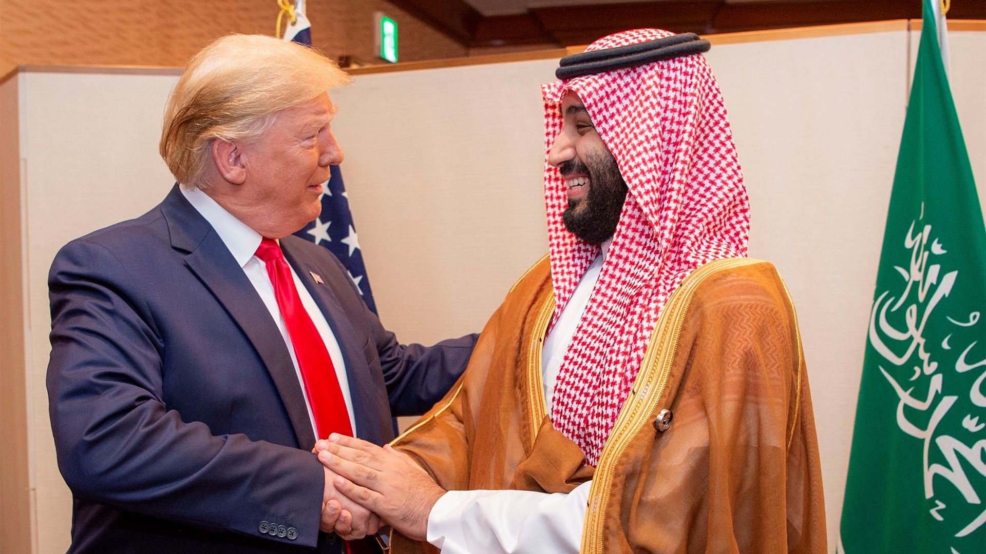 In this image, Trump smiles and shakes hands with MBS.