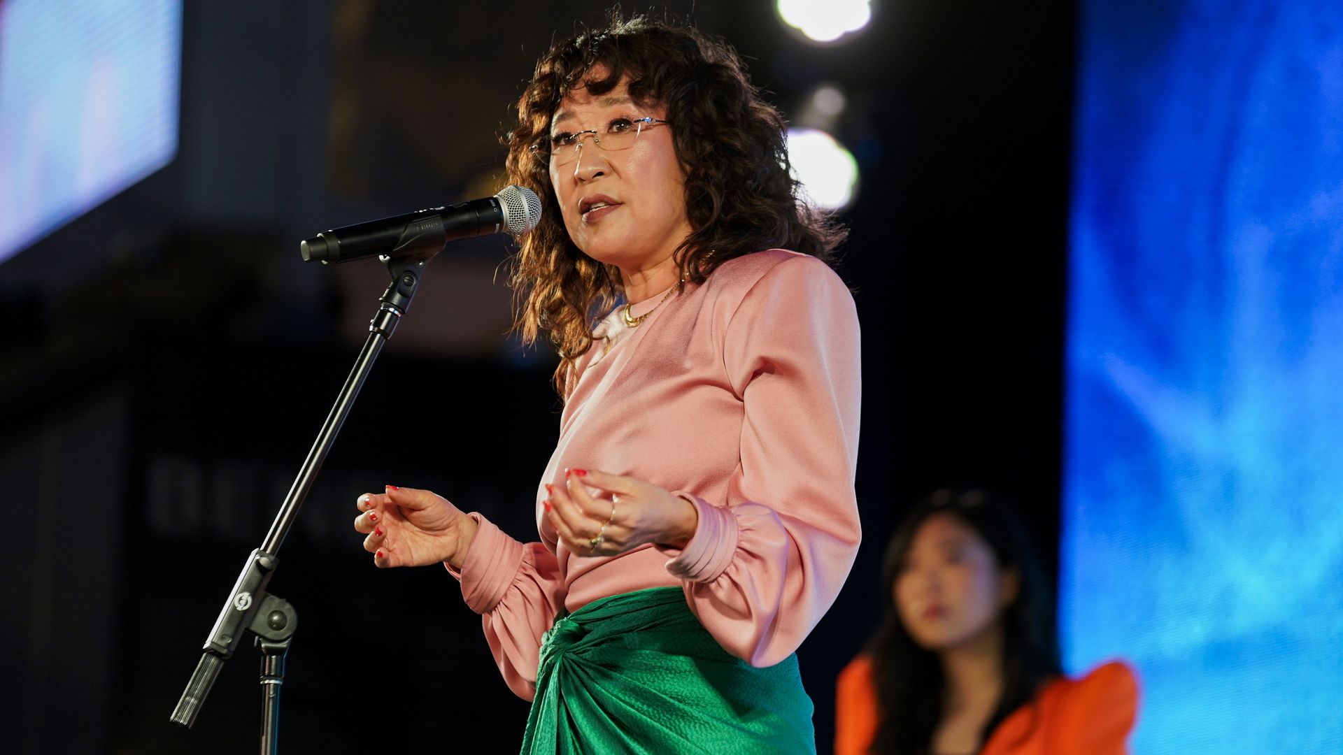 woman on stage giving a speech wearing a white top and green bottoms