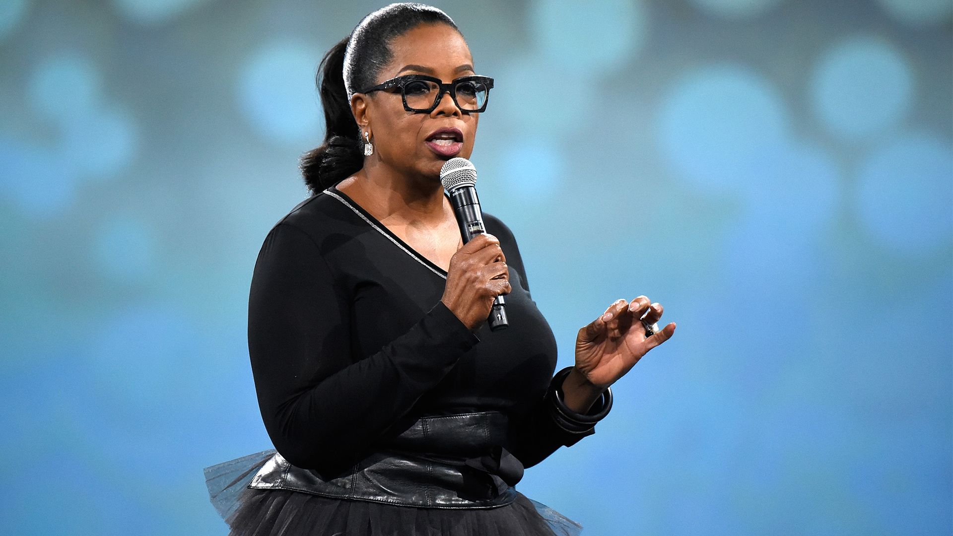 Oprah Winfrey. Wearing black outfit holding microphone.