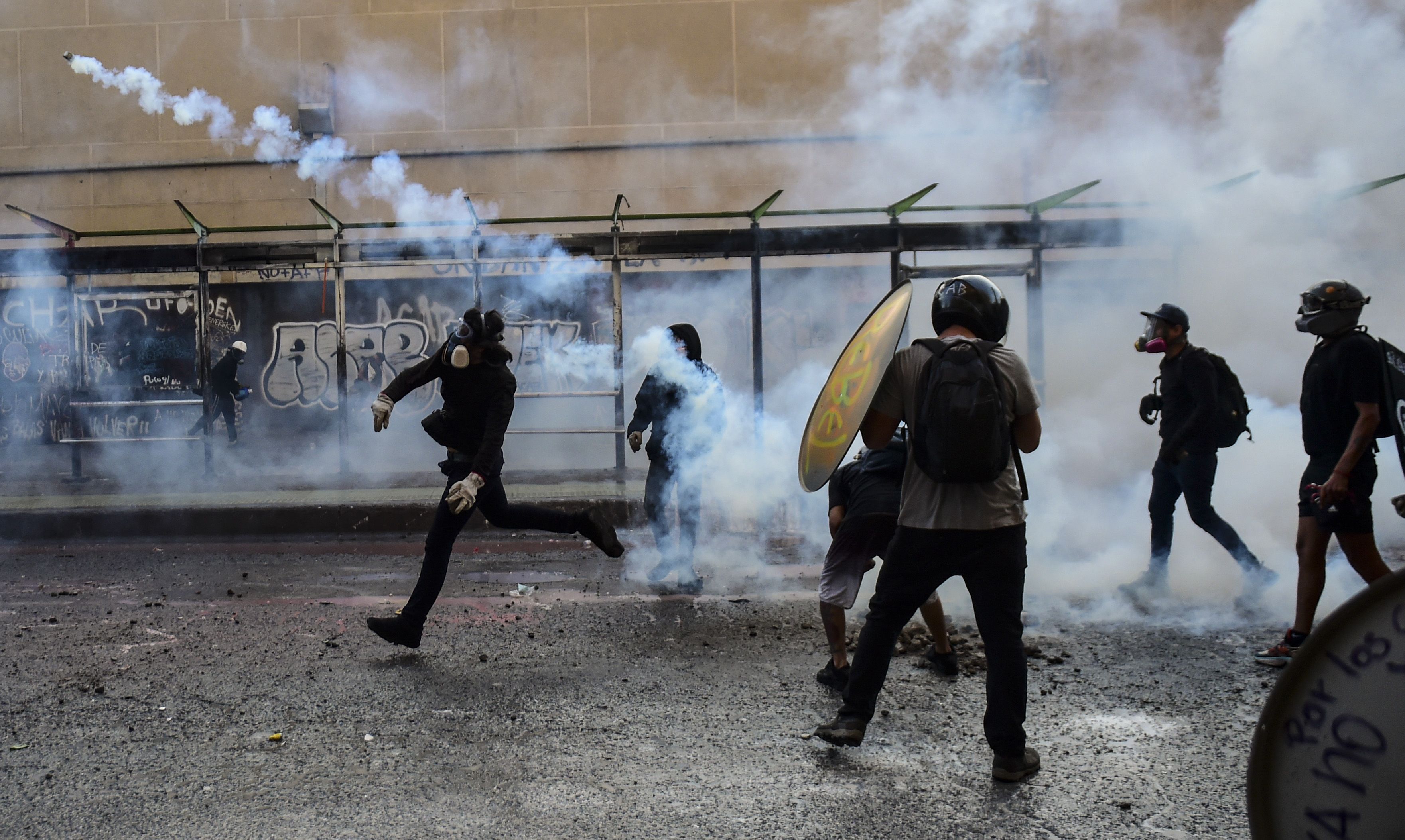 In this image, a protestor throws a tear gas cannister away from other protestors as another holds a shield 