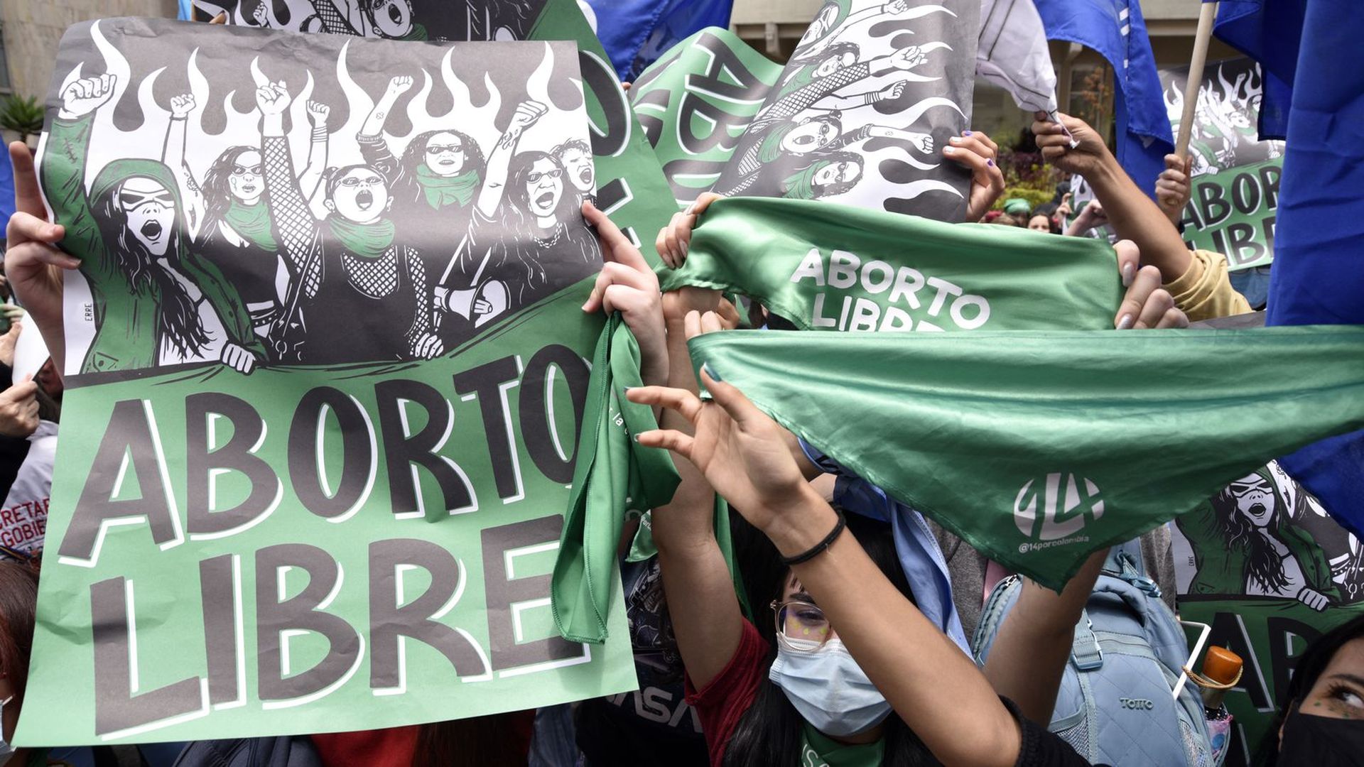 People hold up large green signs that say "free abortion" in Spanish