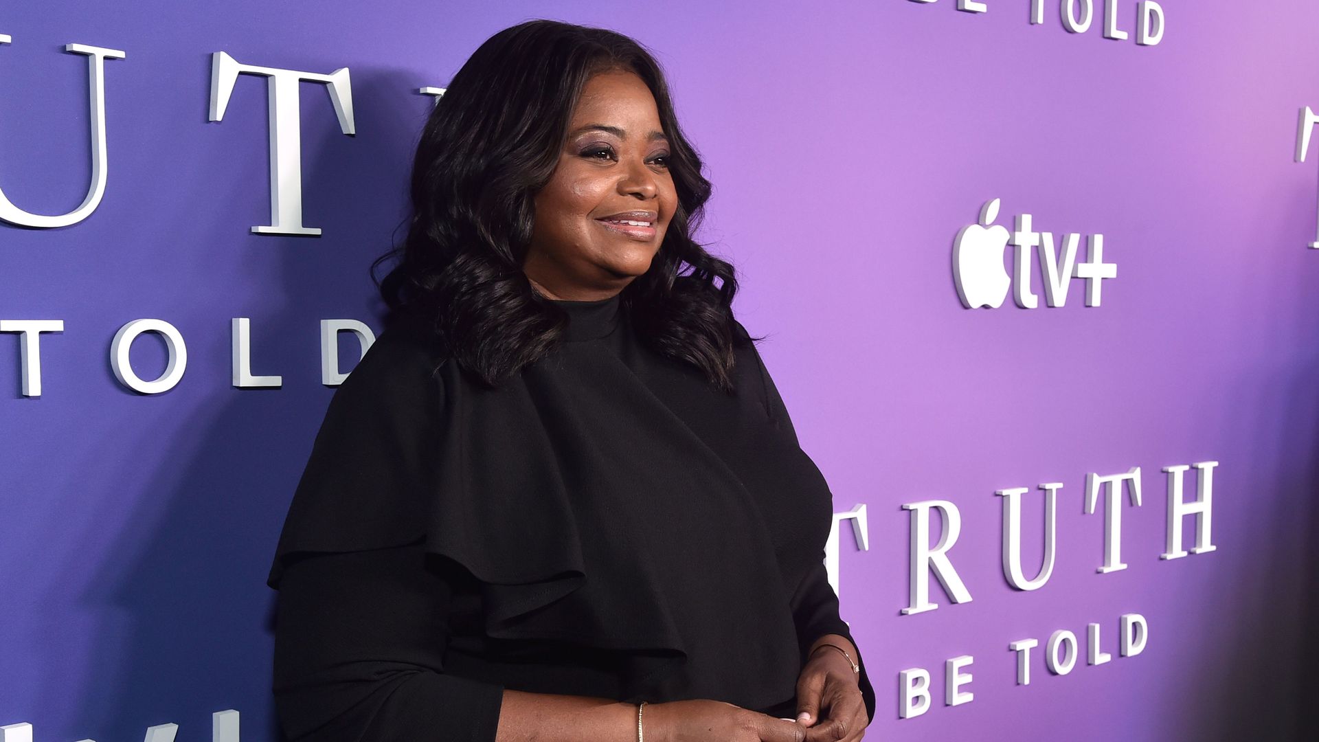 Octavia Spencer smiles on a red carpet in front of a banner that says "Truth Be Told" with Apple TV logos.