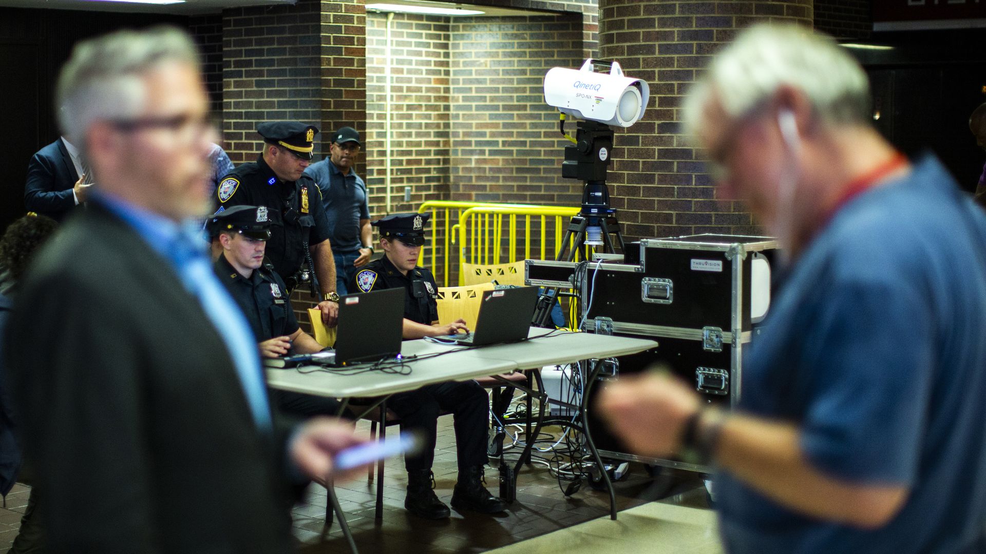 Two men walk by a table as police test body scanning equipment.