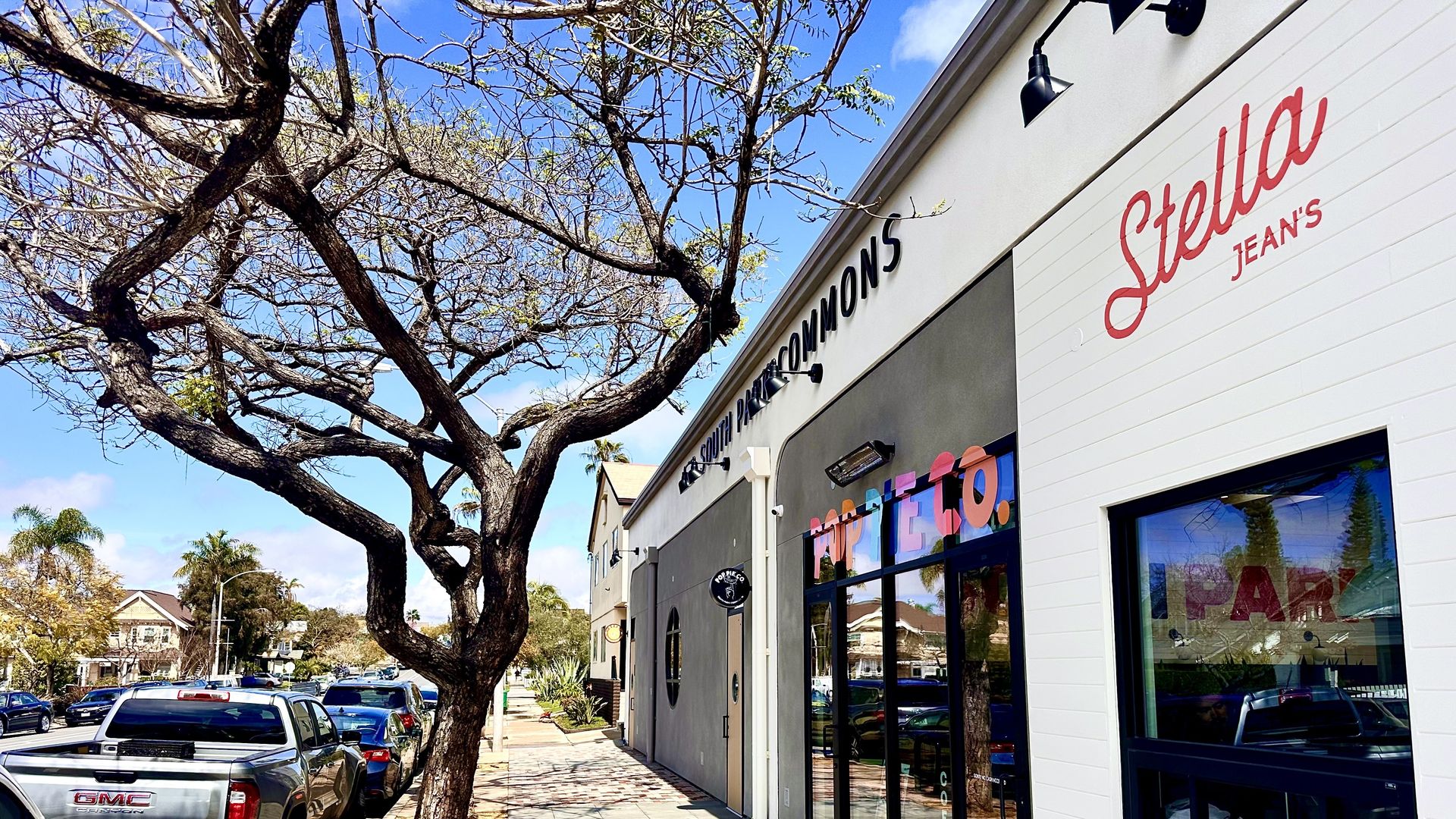 Four restaurants next to a tree without leaves with a blue sky and an empty sidewalk