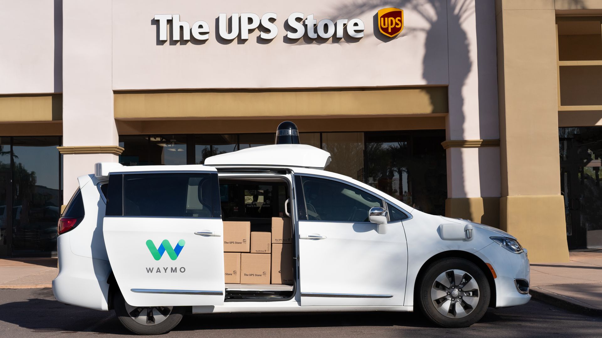 Image of Waymo self-driving minivan loaded with packages in front of UPS Store