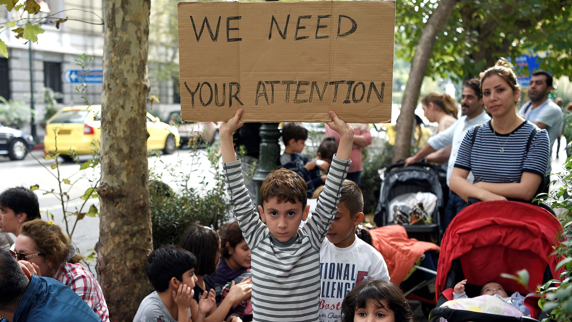 A young boy holds a sign that reads, "We need your attention"
