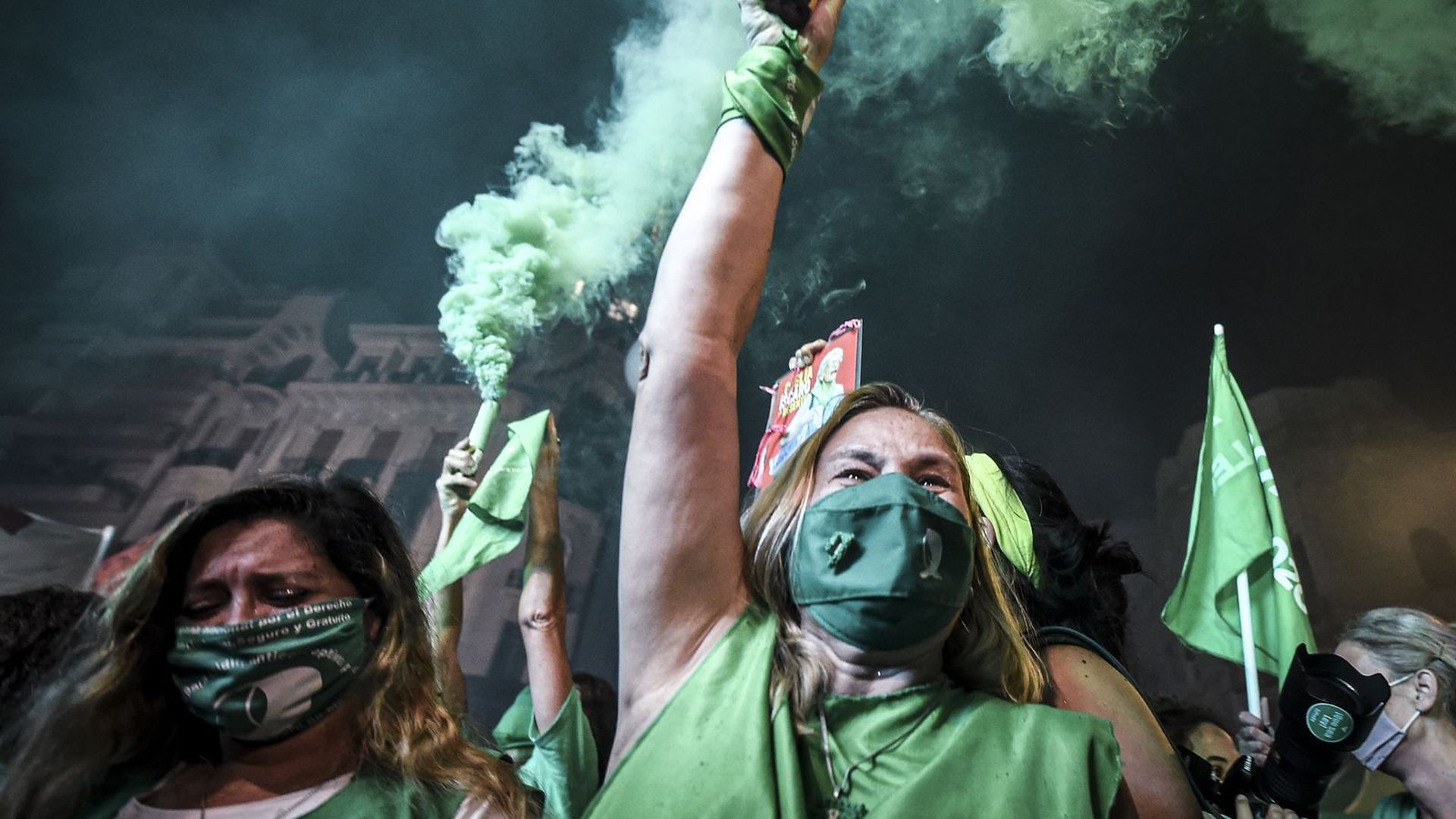 women dressed in all green clothing and wearing green masks celebrate the legalization of abortion in Argentina, waving sticks that emit green smoke in the air 